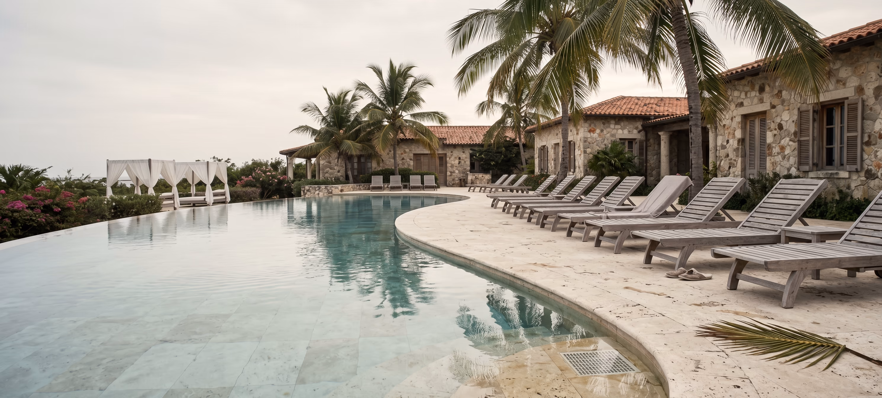 A Caribbean villa pool deck with weathered teak loungers, stone architecture and palm canopies — the destination